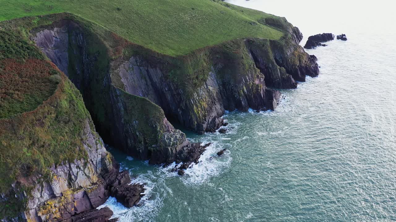 вид с воздуха на красочные изрезанные морские скалы с размытыми фермерскими угодьями в спокойный день на юге ирландии