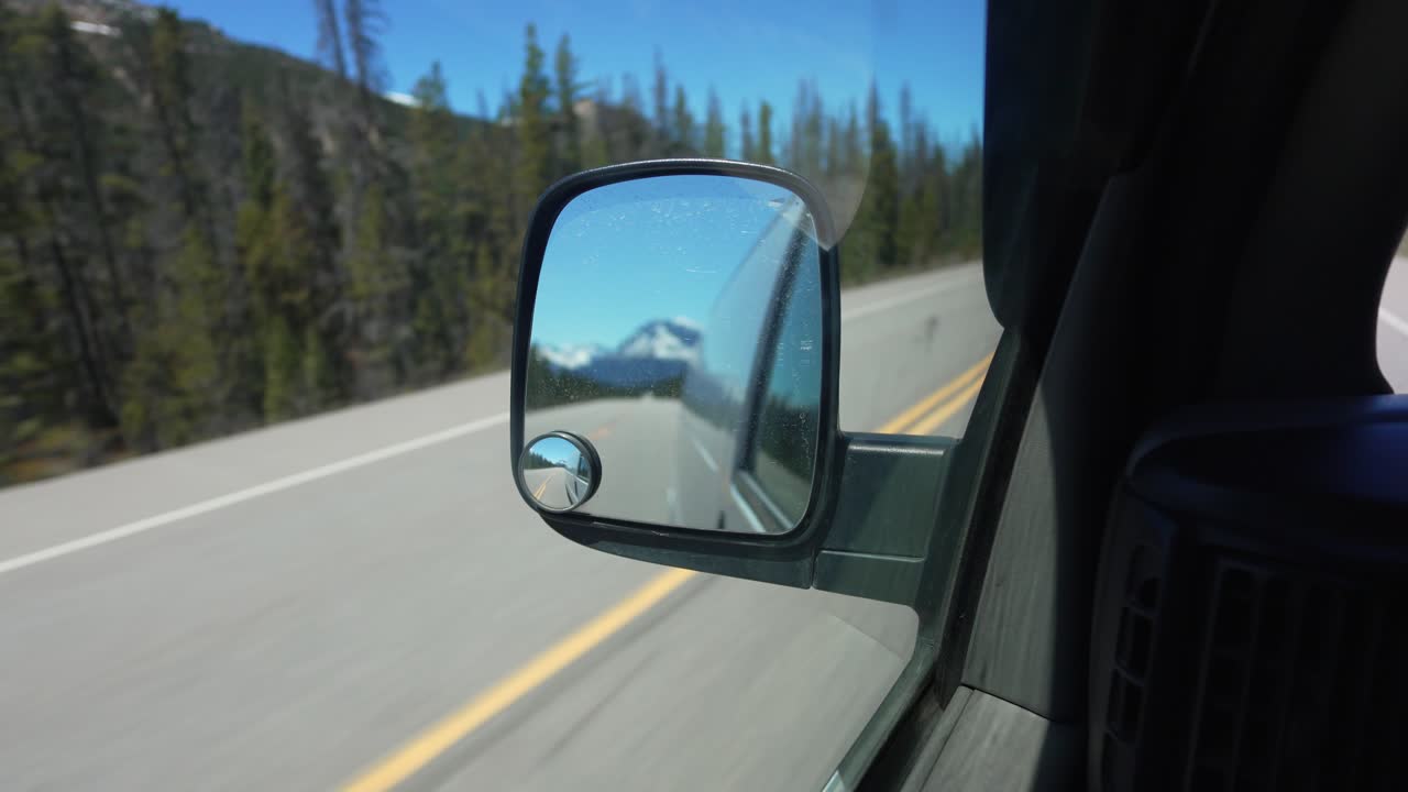 Guidando attraverso le Montagne Rocciose canadesi con le montagne che si riflettono nello specchietto dell'auto.