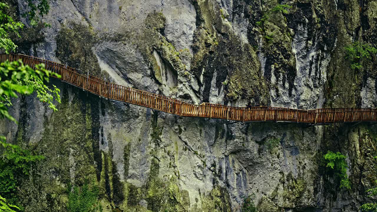 A woman walks along a narrow wooden boardwalk that clings to the side of a steep cliff.The dramatic and adventurous scene . 8k