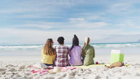 happy group of diverse female friends having fun, sitting on blankets at the beach