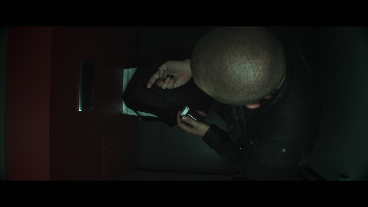 A bald dangerous looking man unpacks a black bag in the public toilet