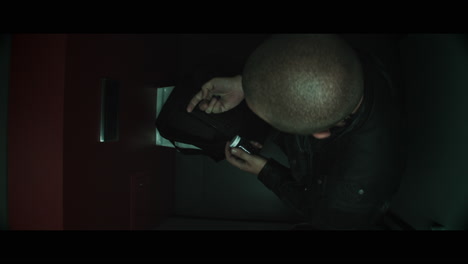 a bald dangerous looking man unpacks a black bag in the public toilet