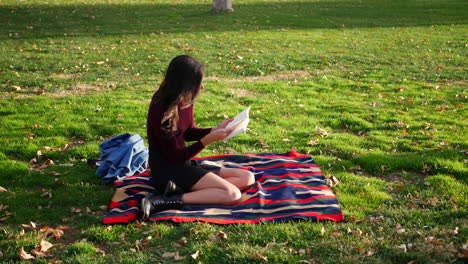 Beautiful-young-hispanic-woman-college-student-reading-a-book-outdoors-in-the-grass-before-class-on-campus