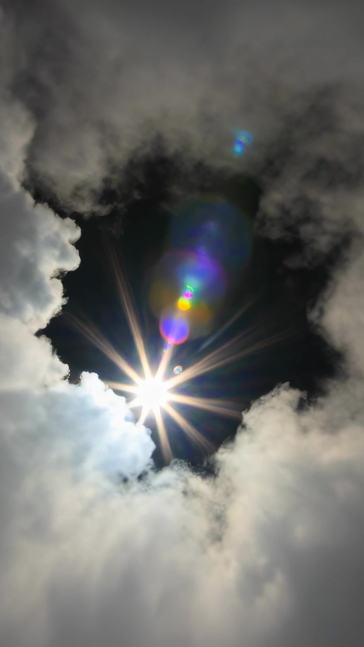Video vertical: Apertura en los cúmulos que revela el sol en lo alto mientras las nubes se desplazan, con destello de lente.