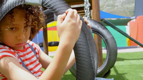 Side-view-of-thoughtful-mixed-race-schoolgirl-sitting-in-a-swing-at-school-playground-4k