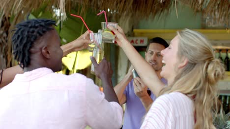 Happy-diverse-group-of-friends-talking-and-making-a-toast-with-cocktails-at-beach-bar