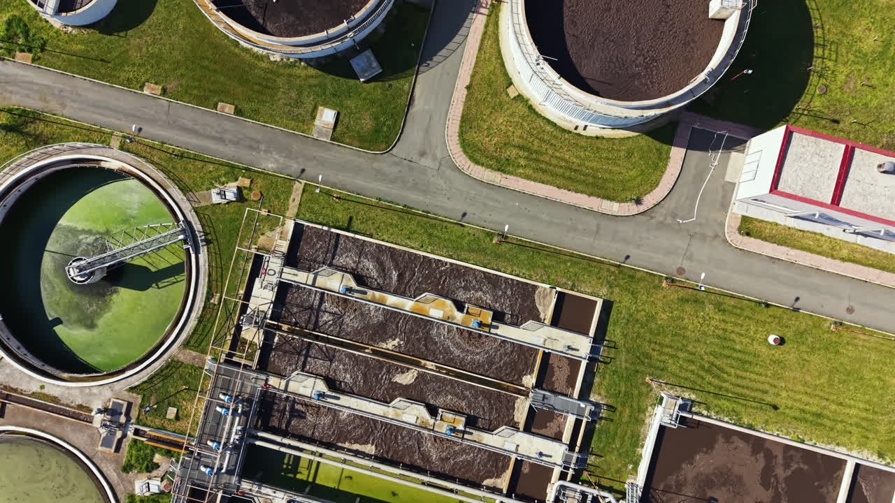 City wastewater treatment plant shows large tanks and processing systems on a sunny day from an aerial view