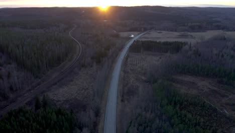 reversed drone footage flying over a country road with cars driving on it during sunset