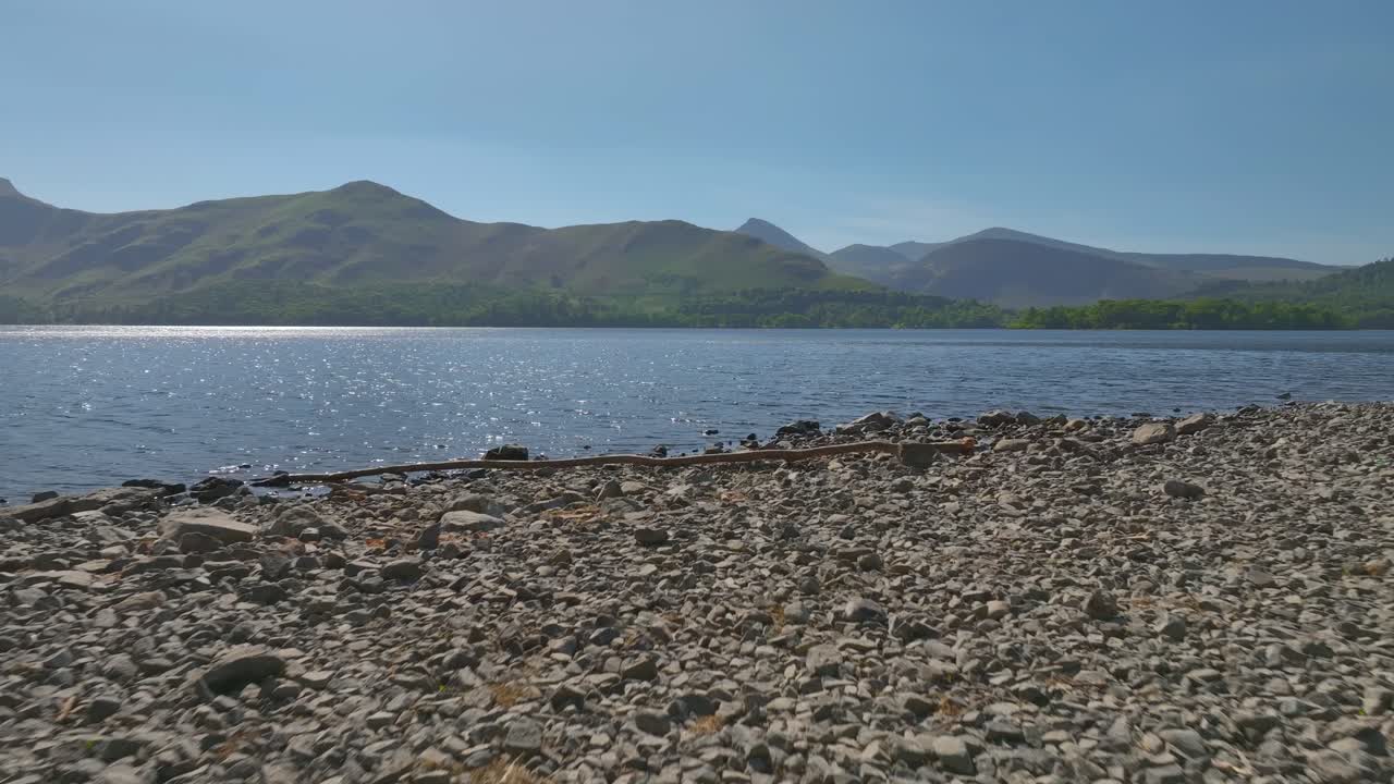 Man alone on lake shore with mountains in the distance. Slow drone flypast to lake. Derwentwater, Lake District, Cumbria, UK.
