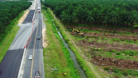 Luftdrohne-Fliegt-Um-Sabrang-Estate-Sime-Darby-Plantage-Herum,-Blühende-Palmenfarm-In-Teluk-Intan-Entlang-Der-Westküstenschnellstraße-E32,-Interstate-Highway,-Bagger,-Der-Den-Hain-Entfernt,-Perak