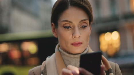 Young-Caucasian-businesswoman-texting-on-her-smartphone-in-the-street-with-city-lights-on-the-background