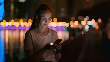 Eine-Junge-Touristin-Reist-Durch-Die-Nächtliche-Großstadt-Und-Schreibt-Textnachrichten-In-Sozialen-Netzwerken-über-Die-Reise,-Hält-Das-Telefon-In-Der-Hand-Und-Schaut-Auf-Den-Bildschirm-Des-Geräts