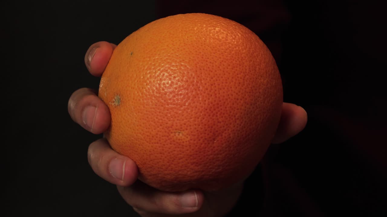 A hand holding a fresh, ripe orange, showcasing its vibrant texture and natural skin. Perfect for illustrating healthy eating, vitamin C-rich fruits, and refreshing natural produce.
