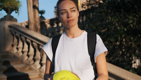 camera zooming on soccer woman with backpack playing with a ball in hands.