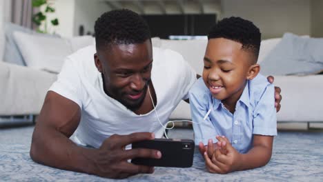 African-american-father-and-son-wearing-earphones-and-using-smartphone-together