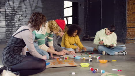 young environmental activists painting placards sitting on the floor