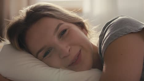 mujer caucásica acostada en la cama por la mañana y mirando a la cámara.