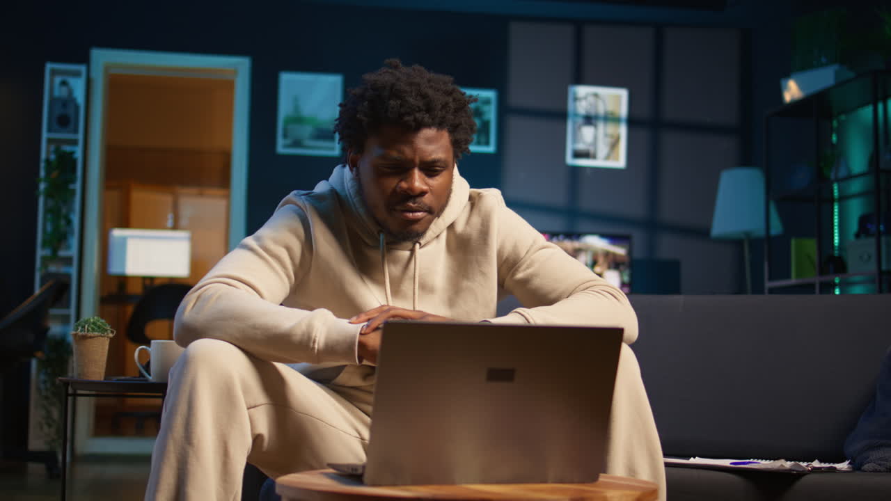 Focused man engaged in online research for a work project at home, sitting at his coffee table with laptop and reading articles on the internet. Person surfing webpages and gathering data. Camera B.