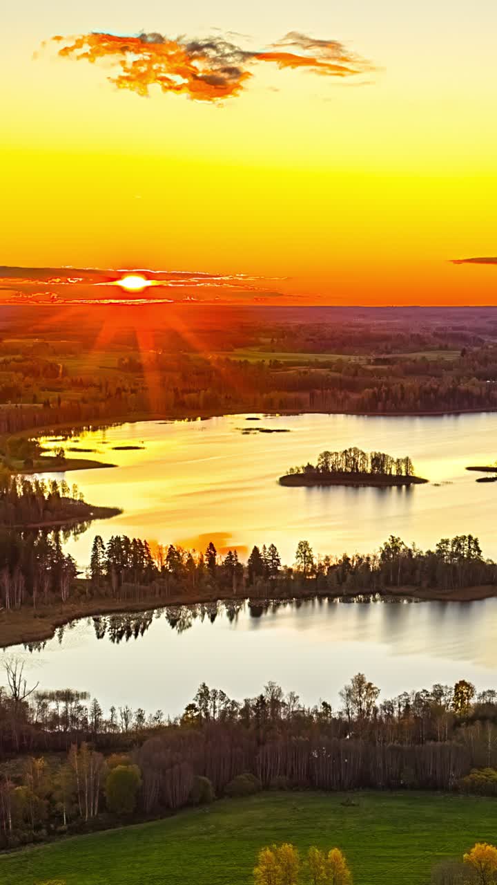 Kultainen auringonnousu mutkittelevan järven yllä pienine metsäisine saarineen ja heijastuksineen, punaisine lämmittävine säteineen nouseva aurinko, pystysuuntainen tausta