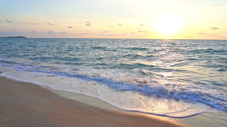 Gros plan sur des vagues déferlant sur une plage tandis que le soleil se couche le long de l'horizon océanique.