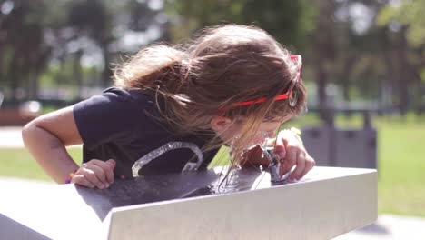 la niña se lava la cara y bebe agua fresca de una fuente de agua potable, en un caluroso día de verano-1