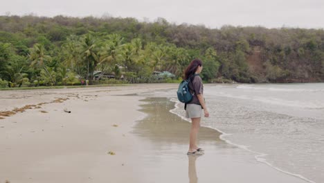 Woman-walking-alone-on-Grand-Anse-Beach-in-Grenada,-calm-day-with-soft-waves-and-tropical-backdrop