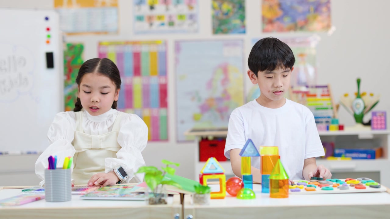 明るく均一な照明が当たる教室のテーブルで、カラフルなブロックの構造物を作る2人の小学生。