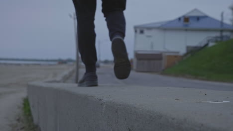 caucasian male walking along a concrete ledge next to the beach on a cool day