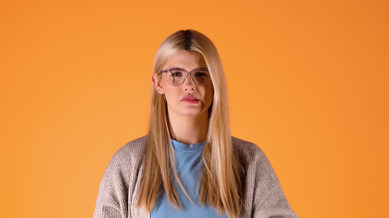 Blonde Young Woman Cries sadly looking at camera and wondering, studio chroma shot, glasses and red rouge lipstick, smart