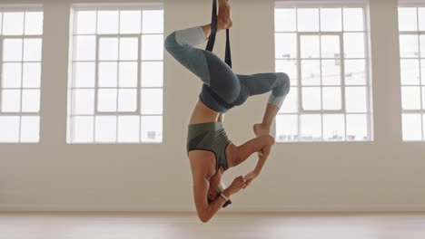 aerial yoga woman practicing bound one-legged king pigeon pose hanging upside down using hammock enjoying healthy fitness lifestyle exercising in studio training meditation at sunrise
