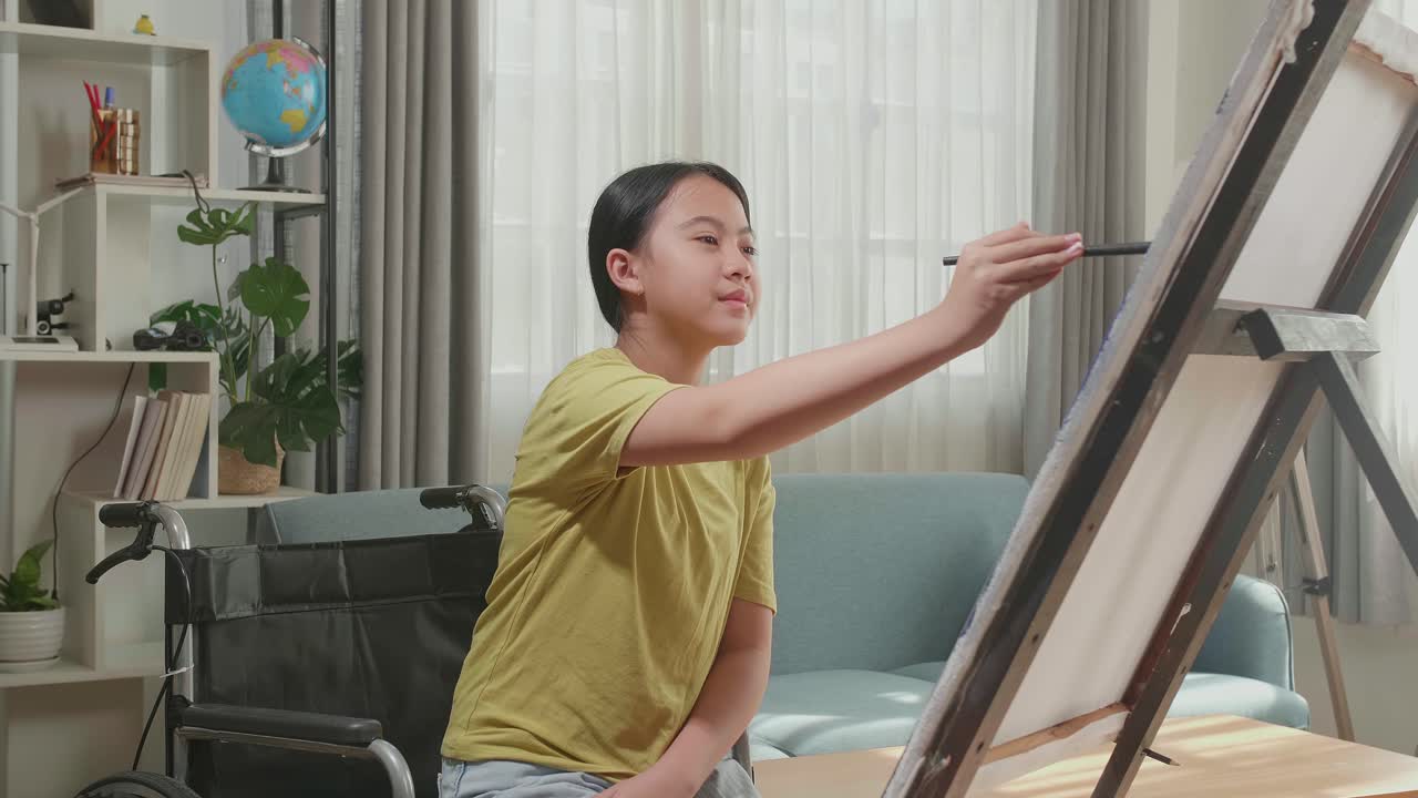 Asian Artist Girl In Wheelchair Holding Paintbrush And Painting On The Canvas