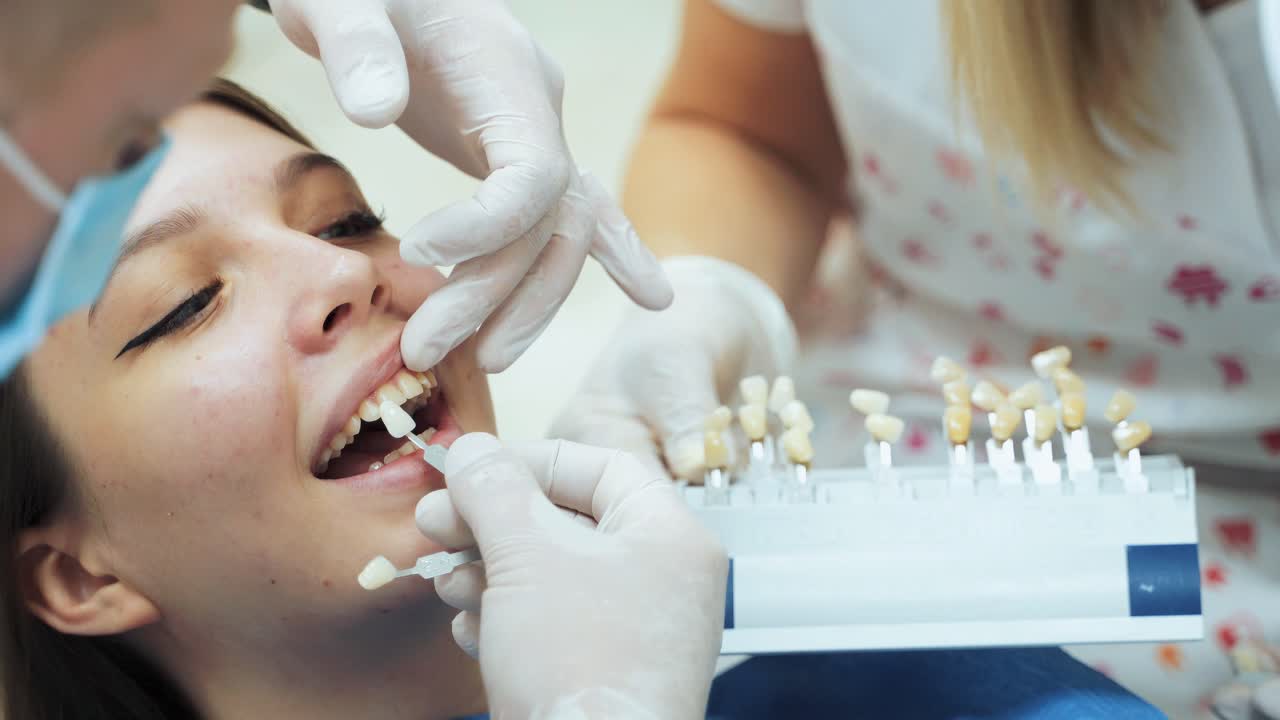 A dentist in rubber white gloves picks up the patients dentures by color. Assistant holds dental samples. Dental clinic