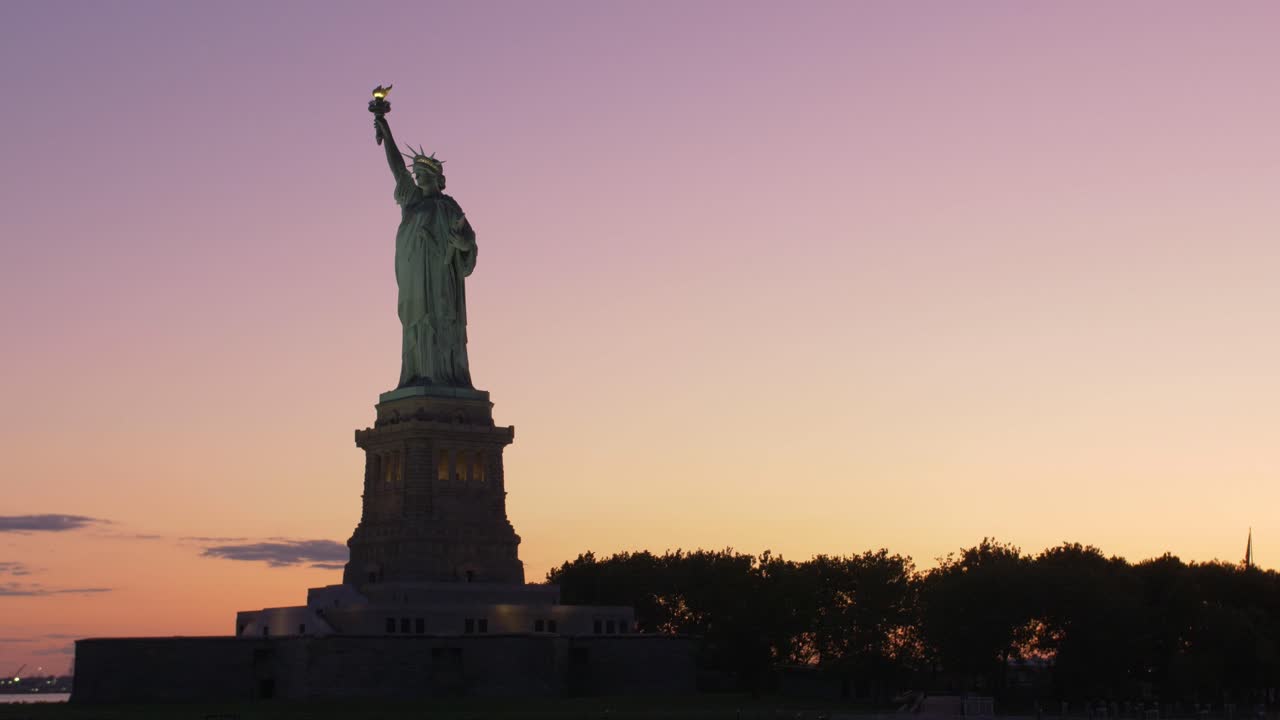establecimiento de una toma de la silueta de la estatua de la libertad al amanecer, tomada desde un bote con fondo naranja y violeta