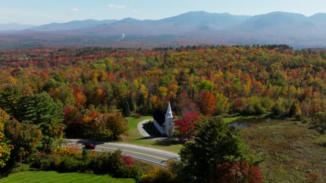 Car-passing-by-a-church-in-New-Hampshire-surrounded-with-fall-foliage-from-an-aerial-view