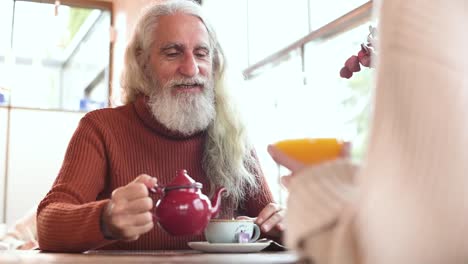 Smiling-senior-man-speaking-with-crop-partner-in-cafe