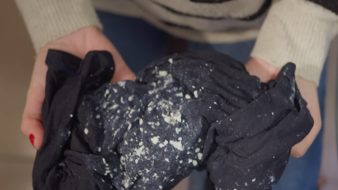 Persona che Mostra un Tessuto Scuro Coperto di Pelucchi Bianchi Dopo il Lavaggio