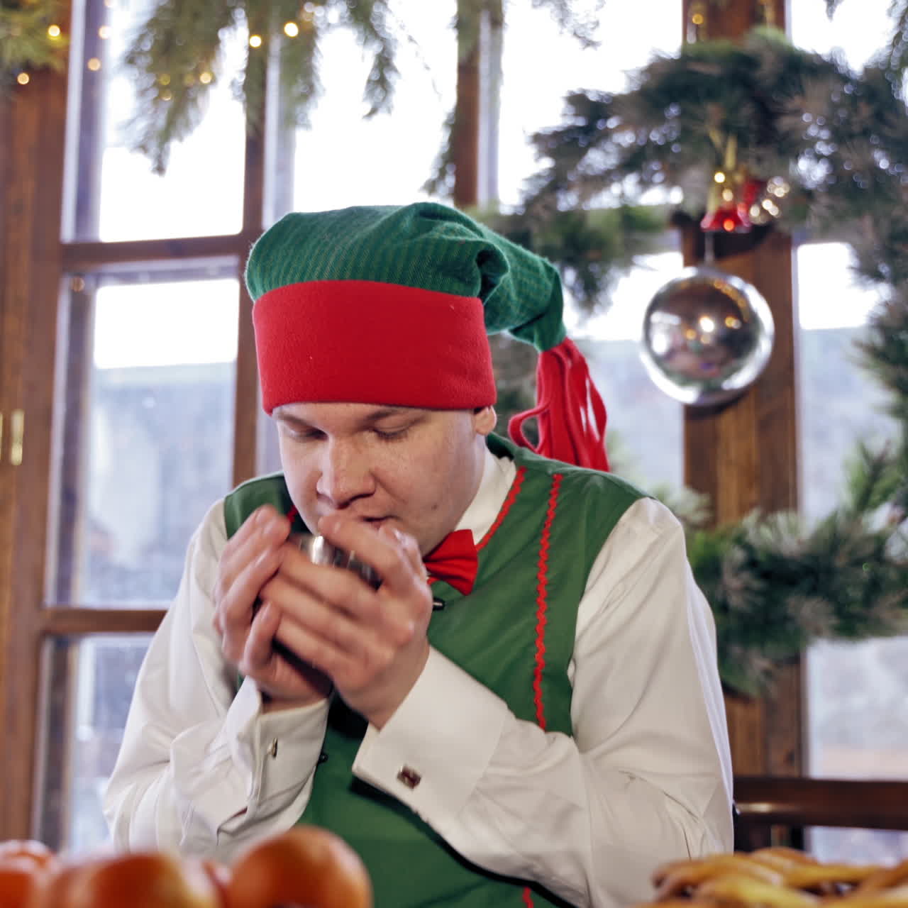 Elf drinking tea at a table. Santas elf drinking Christmas tea in a decorated room. Closeup.