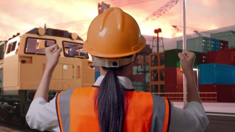 close up back view of a female engineer with safety helmet raising her hands celebrating while working with freight cargo train at port