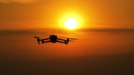 silhouette drone rising with a vibrant orange sunset sky background with clouds