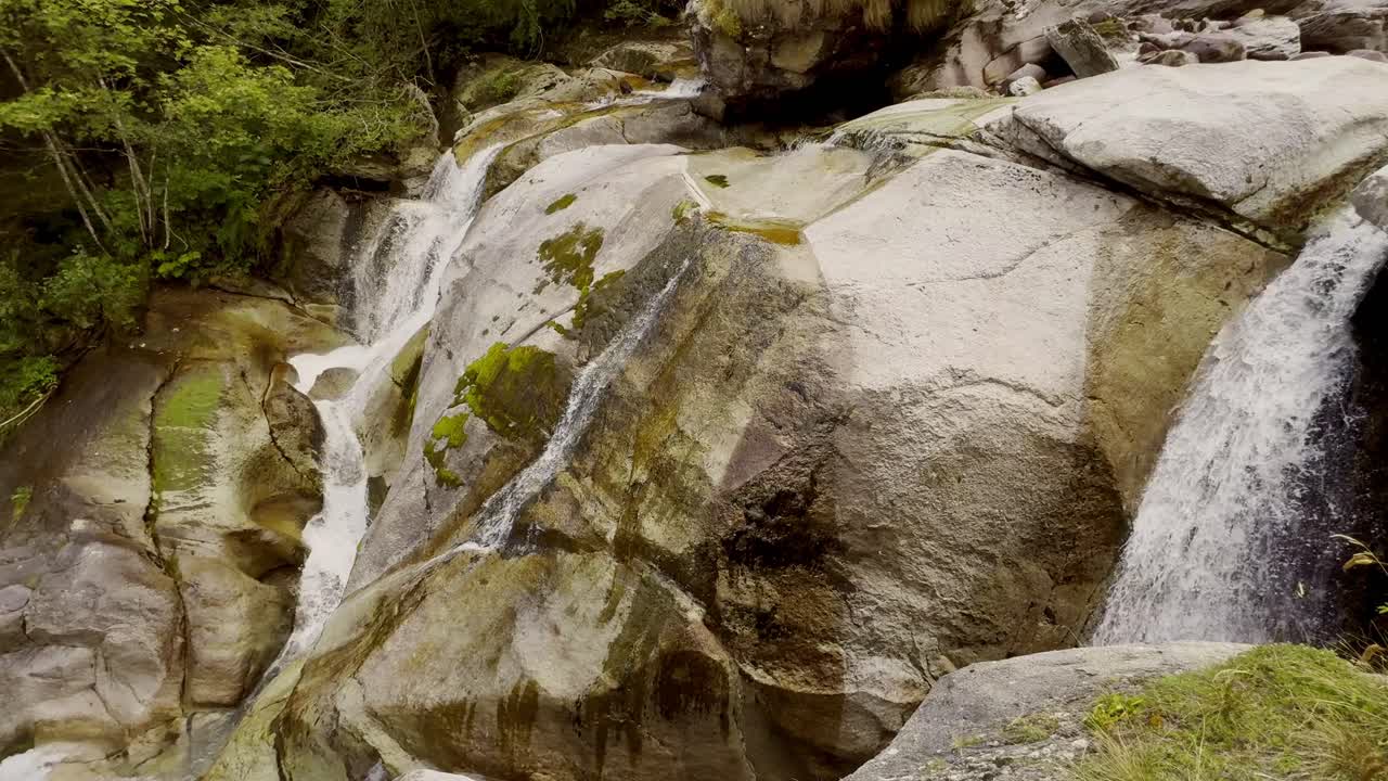 The clip shows a series of small waterfalls and cascades flowing over large, smooth rocks in a natural setting. The rocks are predominantly light grey and beige,