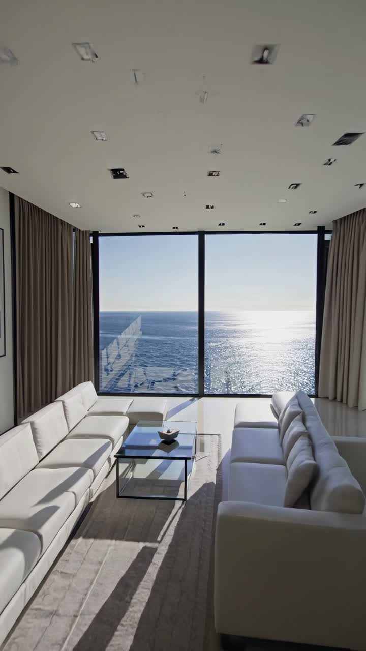 Vidvinkelvideooptagelse af en moderne, minimalistisk stue med panoramaudsigt over havet