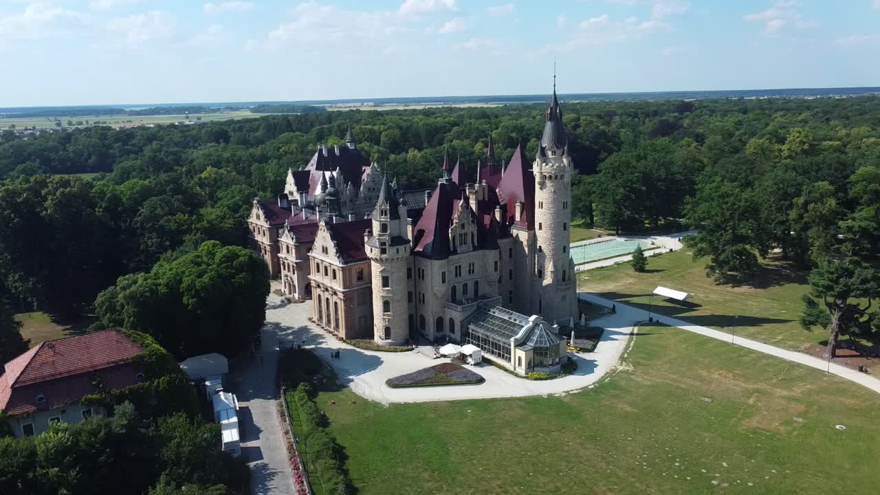 Wide aerial establishing orbit of Moszna Castle, Poland with green gardens and long symmetrical paths