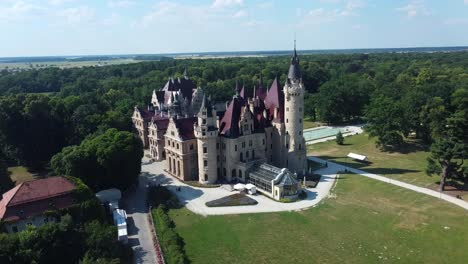 wide aerial establishing orbit of moszna castle, poland with green gardens and long symmetrical paths