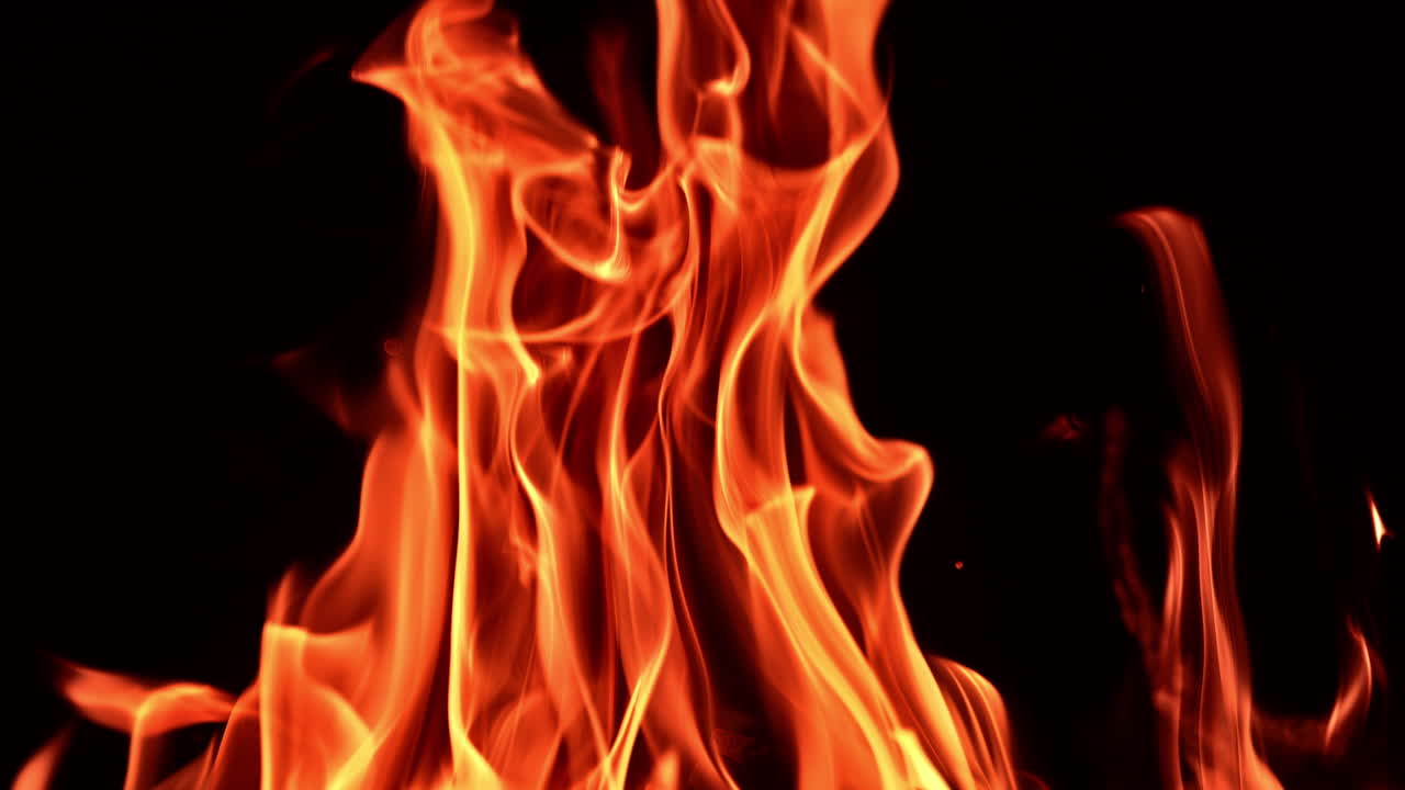 Beautiful flame of fire striving up in the darkness. Upper part of burning bonfire at black backdrop. Close up.