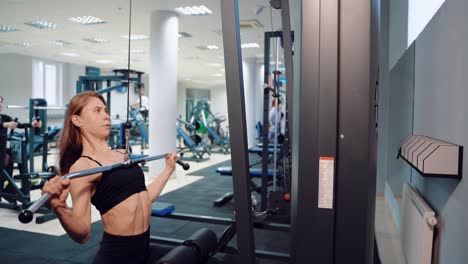 a pretty athlete with loose hair performs an exercise to strengthen the pectoral muscles, surrounded by professional sports equipment in the gym.