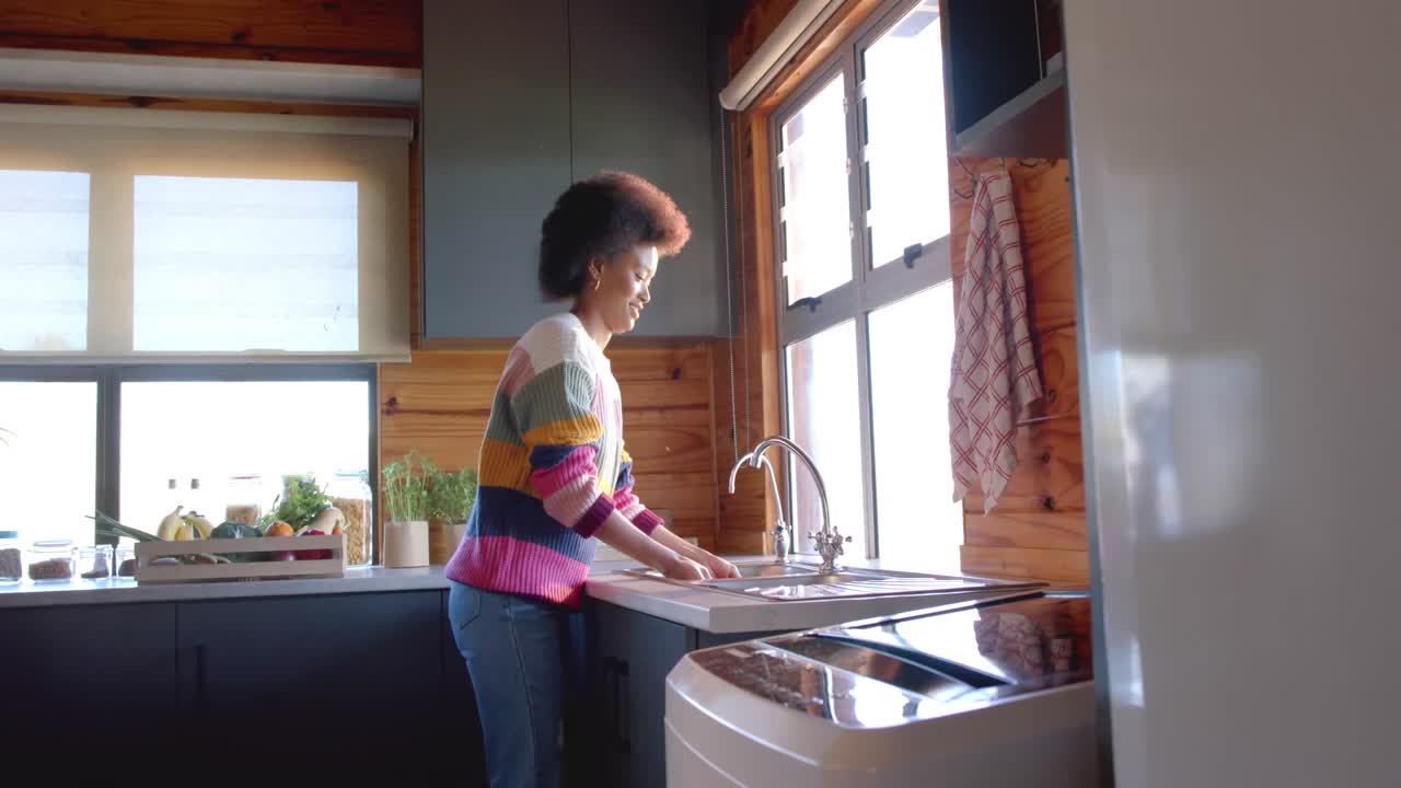 feliz mujer afroamericana enjuagando verduras en una cocina soleada, en cámara lenta