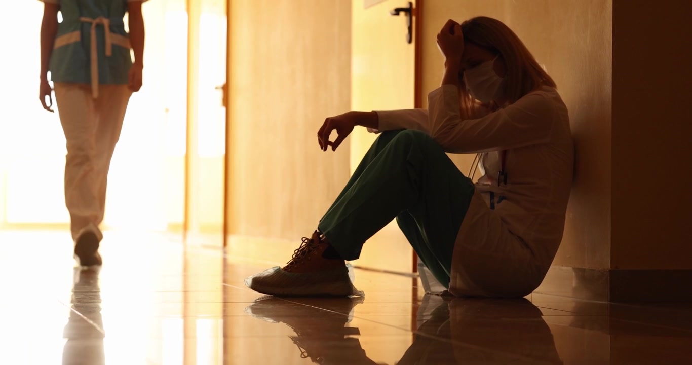 Despaired doctor cries sitting on floor in hospital corridor