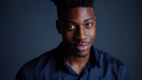 hombre de negocios afroamericano confiado con camisa formal, sonriendo cálidamente mientras hace contacto visual directo contra el fondo azul oscuro del estudio