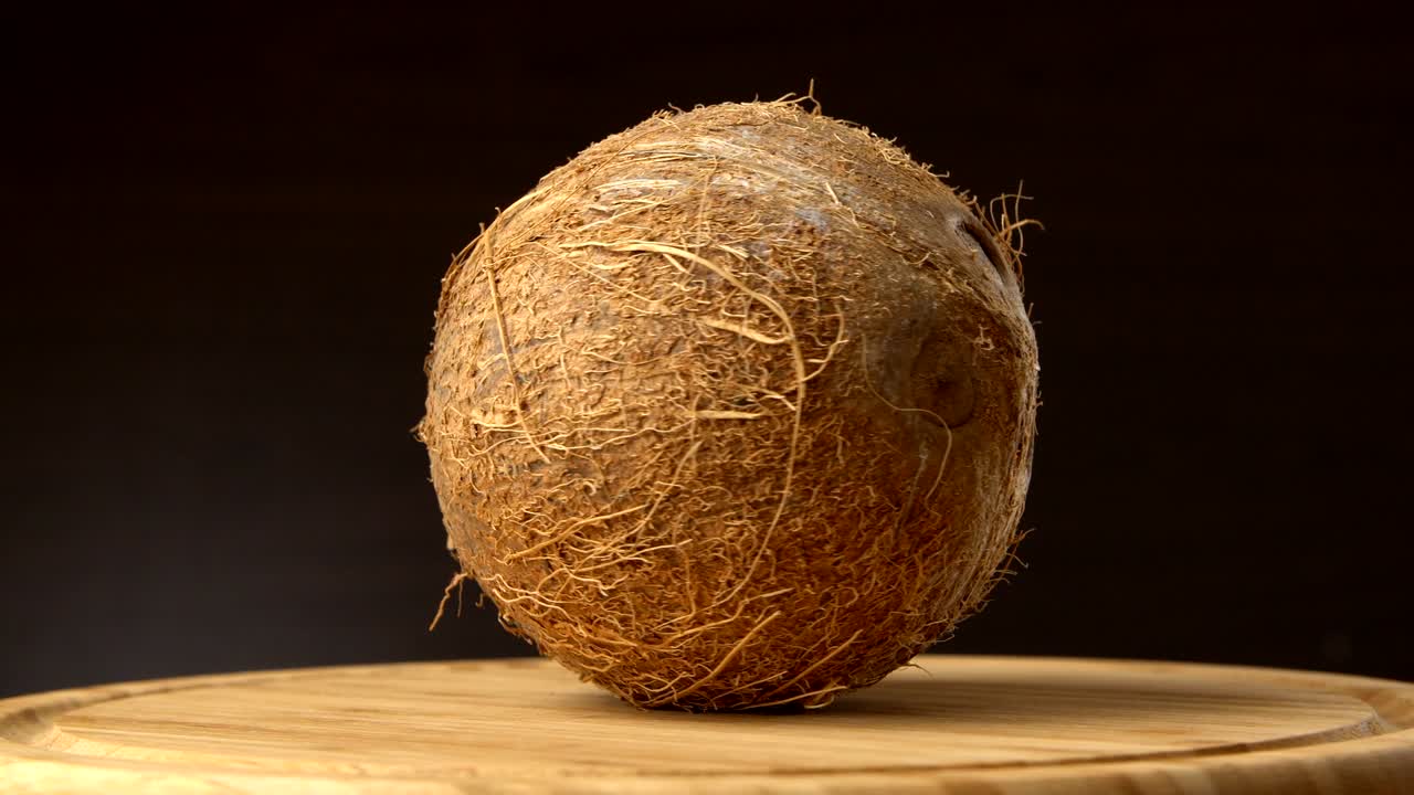 coco tropical maduro girando sobre una mesa de madera contra un fondo negro. frutas tropicales, en bucle