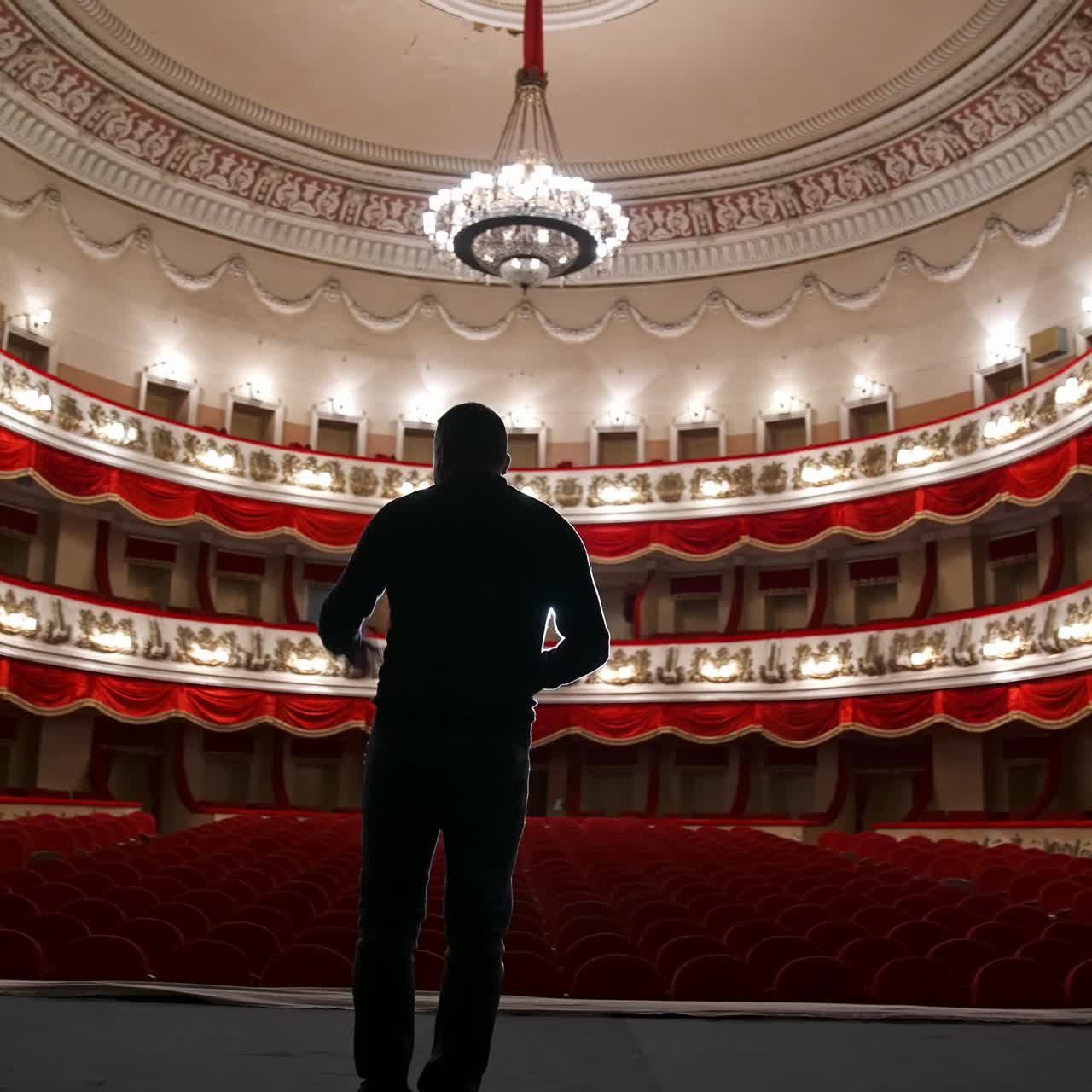 Man on stage on classical theater hall background. Rehearsal before the performance. Actor is talking to the empty auditorium. View from scene